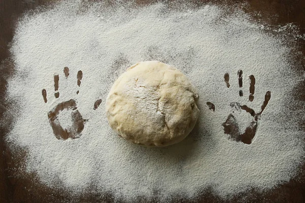 Hands print in flour and raw ball of dough. Both hands print on floured wooden surface and fresh yeast dough for baking.