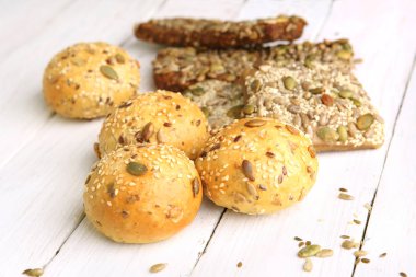 Beyaz ahşap masa üzerinde çeşitli tohum ile ekmek buns. Ekmek rulo ve breadsticks susam, kabak, ayçiçeği, keten tohumu.