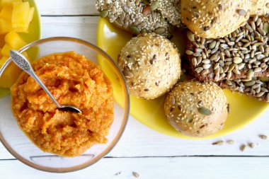 Çeşitli tohum ve beyaz tahta masada kase kabak dip ile ekmek buns. Ekmek rulo ve breadsticks ile susam, kabak, ayçiçeği, keten tohumu ve sebze sos, üstten görünüm. 