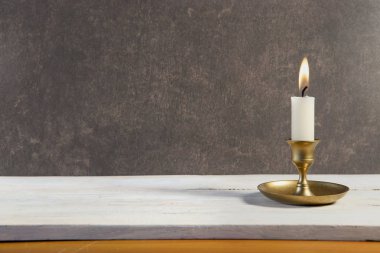 Beyaz ahşap masada eski metal şamdanda yanan mum ve koyu taş arka planda alanı kopyalamak