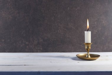 Beyaz ahşap masada eski metal şamdanda yanan mum ve koyu taş arka planda alanı kopyalamak