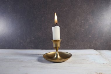 Eskimiş metal şamdanla yanan mum beyaz ahşap masada koyu taş arka planda