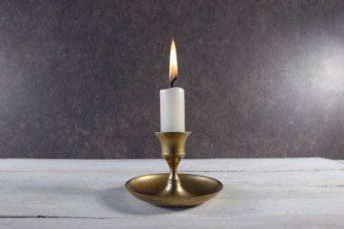 Eskimiş metal şamdanla yanan mum beyaz ahşap masada koyu taş arka planda