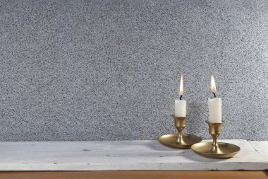 İki mumu eski metal şamdanla beyaz ahşap masada yakmak ve taştan arkaplanda yer kopyalamak.