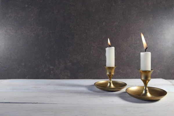 在白色木制桌子上的老式金属烛台上点燃两支蜡烛 并在深色石头背景上复制空间 — 图库照片