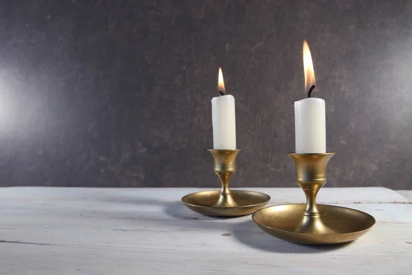 在白色木制桌子上的老式金属烛台上点燃两支蜡烛 并在深色石头背景上复制空间 — 图库照片