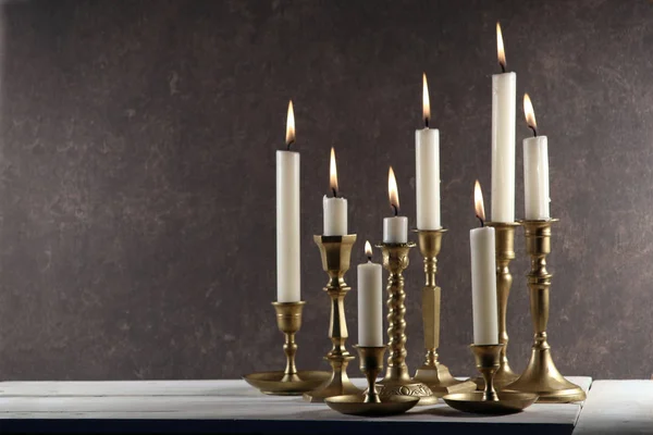 在白色木制桌子上的老式金属烛台上燃烧蜡烛 背景为深色石材 并留有复制空间 — 图库照片