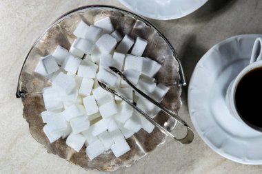 Sugar cubes in metal vintage sugar  bowl with sugar tongs top view.