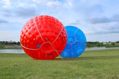 Çim tarlasında iki büyük mavi ve kırmızı zorbing topları. Çayırda büyük plastik kabarcıklar.