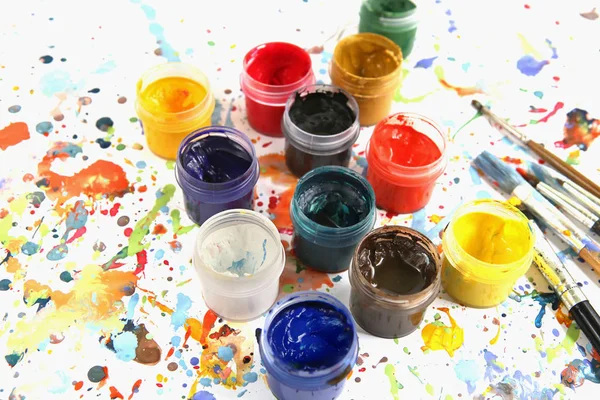 色鮮やかなペイントスプラッシュの背景にグワッシュ塗料やブラシ付きの瓶 図面のためのマルチカラー染料とプラスチック缶 — ストック写真