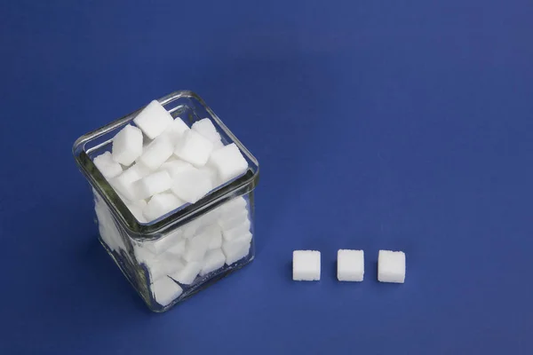 Bir cam kase mavi zemin üzerine beyaz şeker küpleri.