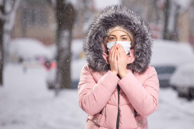 Bulaşıcı hastalıklara karşı korumak için kışın kar altında koruyucu bir maske takan pembe elbiseli kadın portresi. Soğuk algınlığına karşı koruma, grip, hava kirliliği. Sağlık kavramı