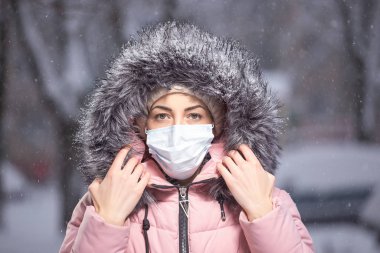 Bulaşıcı hastalıklara karşı korumak için kışın kar altında koruyucu bir maske takan pembe elbiseli kadın portresi. Soğuk algınlığına karşı koruma, grip, hava kirliliği. Sağlık kavramı
