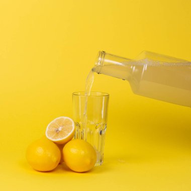 Limon suyu bardağa cam bir şişeyle doldurulur. Limonların tamamı ve kesimi yakınlarda..