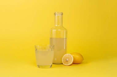 Limon suyu şişesi ve yanında bir bardak ve sarı arka planda izole edilmiş dilimlenmiş limonlar.