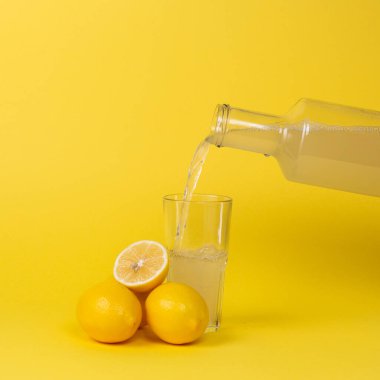 Limon suyu bardağa cam bir şişeyle doldurulur. Limonların tamamı ve kesimi yakınlarda..