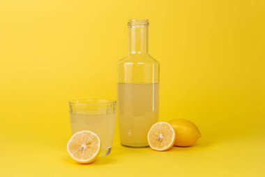 Limon suyu şişesi ve yanında bir bardak ve sarı arka planda izole edilmiş dilimlenmiş limonlar.
