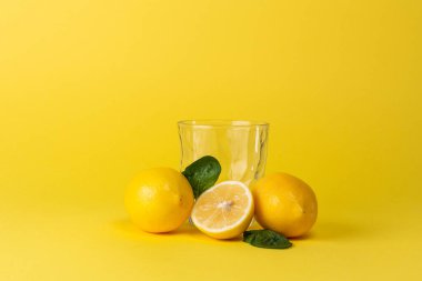 Sarı zemin üzerinde limonlar ve boş cam bardak.