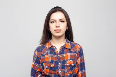 Beyaz-gri arka planda izole edilmiş ekose gömlekle gülümsemeyen güzel bir kadın portresi. Yüzünde asgari doğal makyaj olan bir kız. Fotoğraf cildindeki doğal kusurlarla rötuşlanmamış..