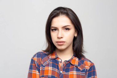 Beyaz-gri arka planda izole edilmiş ekose gömlekle gülümsemeyen güzel bir kadın portresi. Yüzünde asgari doğal makyaj olan bir kız. Fotoğraf cildindeki doğal kusurlarla rötuşlanmamış..