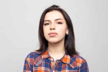 Beyaz-gri arka planda izole edilmiş ekose gömlekle gülümsemeyen güzel bir kadın portresi. Yüzünde asgari doğal makyaj olan bir kız. Fotoğraf cildindeki doğal kusurlarla rötuşlanmamış..