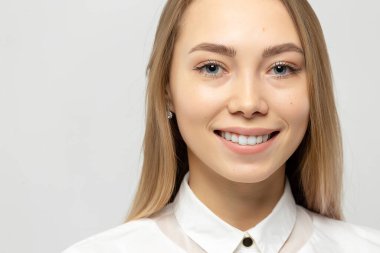 Güzel, mutlu, beyaz gömlekli, beyaz tenli, beyaz arka planda kameraya bakan sarışın bir kadının yakın plan portresi.