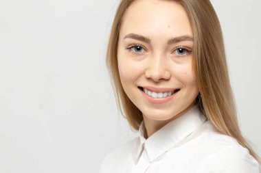 Güzel, mutlu, beyaz gömlekli, beyaz tenli, beyaz arka planda kameraya bakan sarışın bir kadının yakın plan portresi.