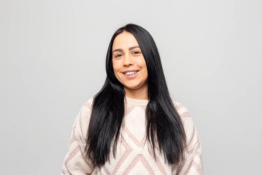 Açık gri arka planda, sıcak kış süveteri giymiş, gülümseyen, güzel, esmer bir kızın portresi..