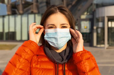 Bir kadın alerji, virüs ve hava kirliliğine karşı koruyucu bir maske takar. İklim değişikliği konsepti. Sokaktaki kırmızı ceketli, Coronavirus 'tan gelen tıbbi maskeli genç bir kadının portresi.