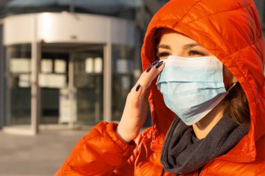 Bir kadın alerji, virüs ve hava kirliliğine karşı koruyucu bir maske takar. İklim değişikliği konsepti. Sokaktaki kırmızı ceketli, Coronavirus 'tan gelen tıbbi maskeli genç bir kadının portresi.