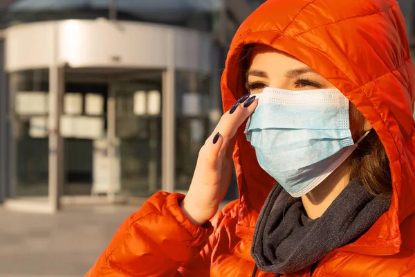 A woman wears a protective mask against allergies, viruses, air pollution. Climate change concept. Portrait of a young woman in a medical mask from a coronavirus in a red jacket on the street