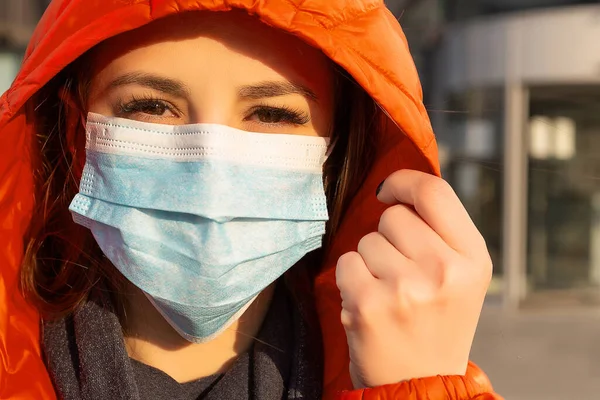A woman wears a protective mask against allergies, viruses, air pollution. Climate change concept. Portrait of a young woman in a medical mask from a coronavirus in a red jacket on the street