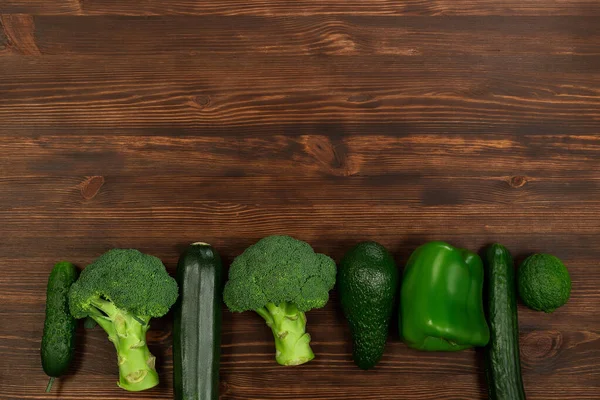 Collection of green vegetables produce on dark background, broccolini, avocado, squash, chilli, grapes part of flat lay overhead set