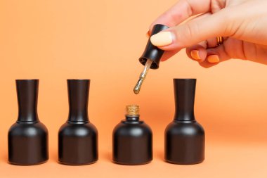 Bej arka planda siyah kavanozlardaki ojeler. Kadın eli, oje sürmek için fırça tutuyor..