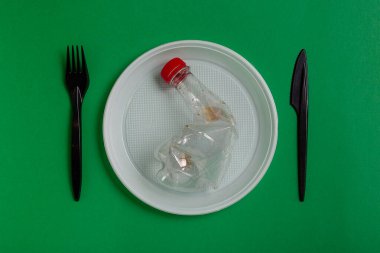 Yeşil arka planda plastik tek kullanımlık aletler. çatal, bıçak, tabak