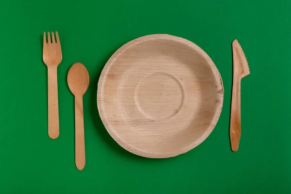 Eco-friendly disposable utensils made of bamboo wood on a green background. Draped spoons, fork, knives, bamboo bowls with.