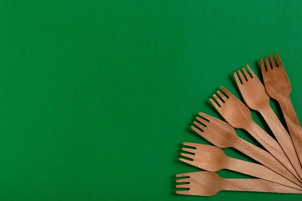 Eco-friendly disposable utensils made of bamboo wood on a green background. Draped spoons, fork, knives, bamboo bowls with.