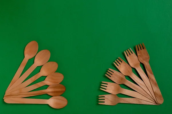 Eco-friendly disposable utensils made of bamboo wood on a green background. Draped spoons, fork, knives, bamboo bowls with.