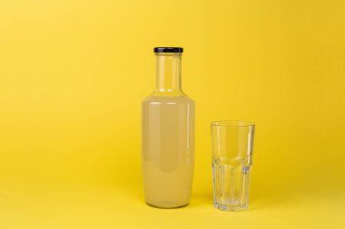 Limon suyu şişesi ve yanında boş bir bardak sarı arka planda izole edilir.