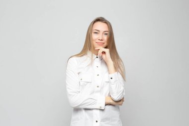 Beyaz gömlekli gülümseyen güzel bir kadının portresi beyaz-gri arka planda izole edilmiş. Yüzünde asgari doğal makyaj olan bir kız. Fotoğraf cildindeki doğal kusurlarla rötuşlanmamış..