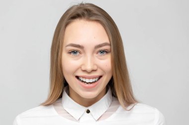 Güzel, mutlu, beyaz gömlekli, beyaz tenli, beyaz arka planda kameraya bakan sarışın bir kadının yakın plan portresi.