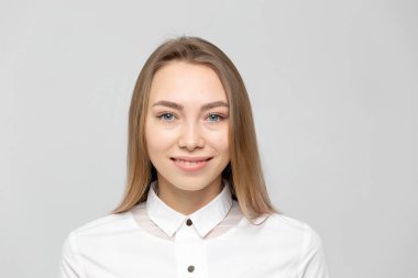 Güzel, mutlu, beyaz gömlekli, beyaz tenli, beyaz arka planda kameraya bakan sarışın bir kadının yakın plan portresi.