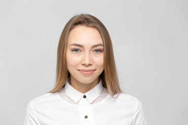 Güzel, mutlu, beyaz gömlekli, beyaz tenli, beyaz arka planda kameraya bakan sarışın bir kadının yakın plan portresi.