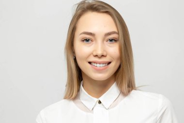 Güzel, mutlu, beyaz gömlekli, beyaz tenli, beyaz arka planda kameraya bakan sarışın bir kadının yakın plan portresi.