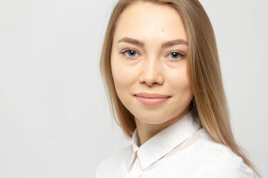 Güzel, mutlu, beyaz gömlekli, beyaz tenli, beyaz arka planda kameraya bakan sarışın bir kadının yakın plan portresi.