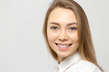 Güzel, mutlu, beyaz gömlekli, beyaz tenli, beyaz arka planda kameraya bakan sarışın bir kadının yakın plan portresi.