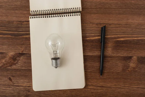 stock image vintage book and light bulb on wood table. notebook, pen lies on a wooden table. idea concept