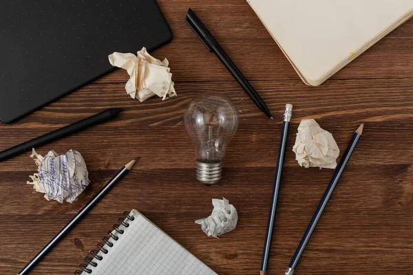 Creative idea inspiration concept by web designer or digital artist. New idea and Innovation with Crumpled Paper light bulb on brown wooden background. Pens, pencils, notebook, graphic tablet on table
