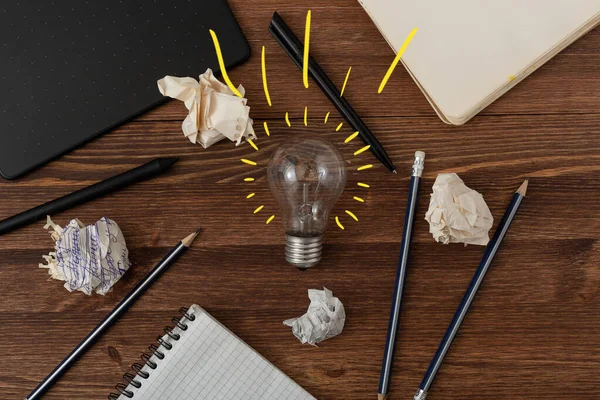 Creative idea inspiration concept by web designer or digital artist. New idea and Innovation with Crumpled Paper light bulb on brown wooden background. Pens, pencils, notebook, graphic tablet on table