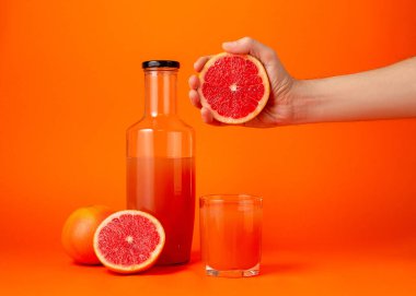 Taze olgun greyfurtun yarısını elinde tutan, turuncu duvarda izole edilmiş cam bardak taşıyan bir kadının kesilen fotoğrafını yakın plan çek. İnsanlar canlı yaşam tarzı tatil konseptini gevşetiyor. Kopyalama alanı oluştur